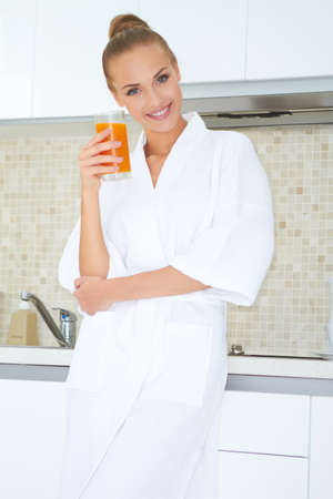 Glamorous woman in a white bath robe enjoying a large glass of fresh orange juice for breakfastの写真素材