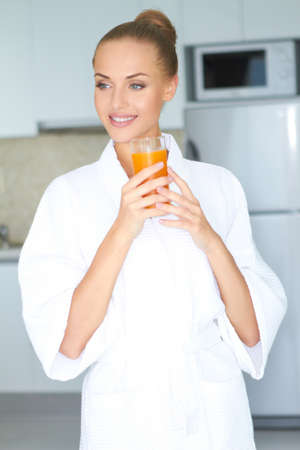 Stylish woman in a thick white towelling gown drinking a large glass of healthy orange juiceの写真素材