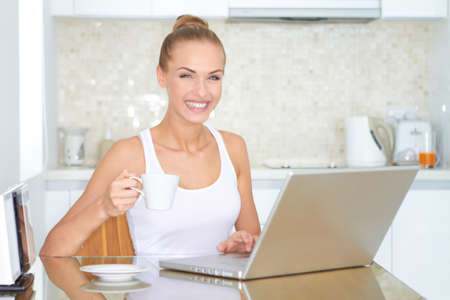 Laughing woman sitting at her laptop computer in her kitchen enjoying something she has just read over the internetの写真素材
