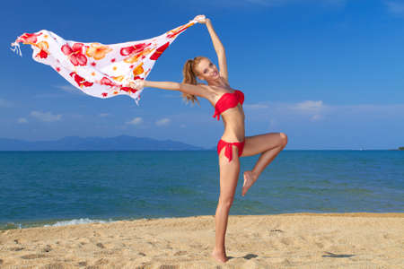 Smiling woman in white bikini holding scarf against blue sky , on beautiful sandy beachの写真素材
