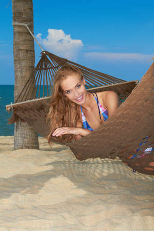 Smiling woman relaxing in a hammock on a sandy beach enjoying an idyllic tropical getawayの写真素材