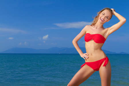 Beautiful smiling woman posing in red bikini with blue sea and sky as a backgroundの写真素材