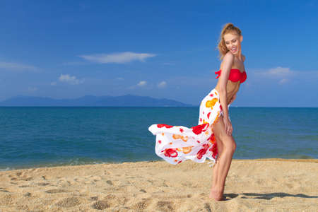 Playful moment with the wind in her sarong entertains a pretty blonde on the beachの写真素材
