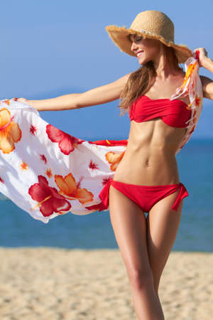 Beautiful blonde in a red bikini letting her sarong flow in the breeze at the oceanの写真素材