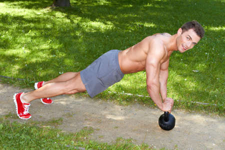 Handsome man exercises with kettlebell in parkの写真素材