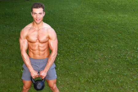 Muscular man holding kettlebell on grass backgroundの写真素材