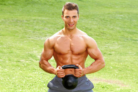 Muscular man holding kettlebell on grass backgroundの写真素材
