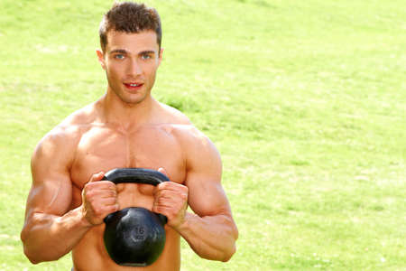 Muscular man holding kettlebell on grass backgroundの写真素材