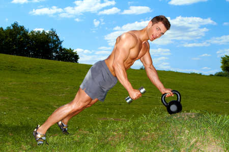 Sporty man practicing with weights at the parkの写真素材
