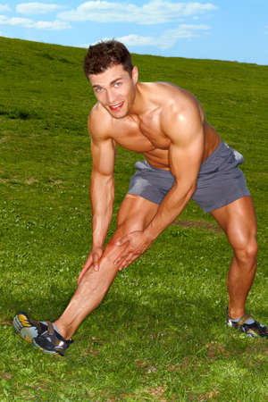 Handsome man doing stretch exercises on grassの写真素材