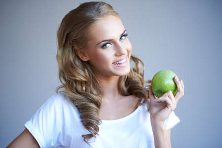 Head shot of woman holding green apple against grey backgroundの写真素材