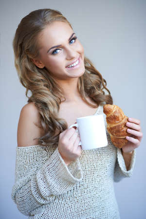 Cute girl holding white cup of hot drink while isolated on grayの写真素材