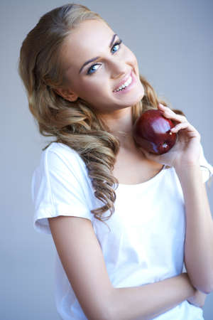 Head shot of woman holding red apple against grey backgroundの写真素材