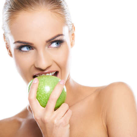 Woman tries to bite a fresh green apple, she is isolated on whiteの写真素材