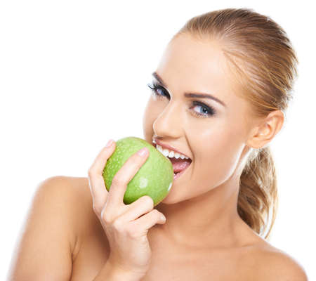 Beautiful  young woman bites a green apple on whiteの写真素材
