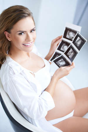 Pregnant woman holding her USG pictures while sittingの写真素材