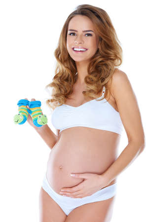 Young happy pregnant woman holding small baby shoesの写真素材