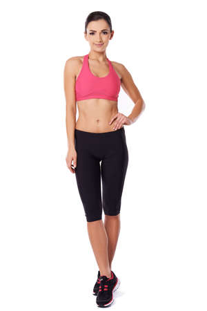 Shapely beautiful fit woman in gym tights posing standing with her hand on her hip, studio portrait over whiteの写真素材