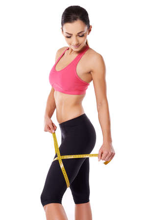 Shapely fit woman athlete measuring her thigh with a tape measure to keep watch on her weight gain or lossの写真素材