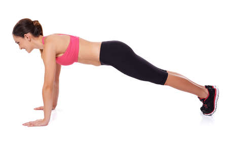 Fit healthy young woman working out in a gym doing press ups, studio portrait over whiteの写真素材
