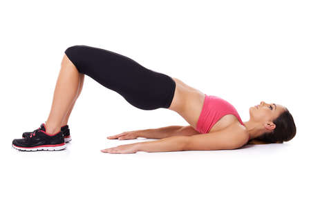 Fit woman doing exercises lying on her back on the floor raising her knees and body in the air, studio over whiteの写真素材