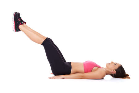Woman doing leg lifts to strengthen her abdominal muscles while lying on the floor working out, studio portrait over whiteの写真素材
