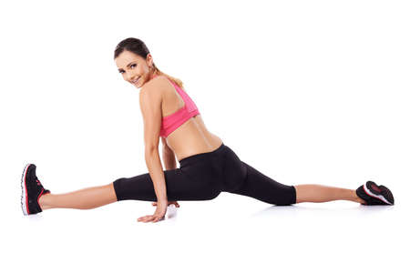 Pretty smiling woman doing the splits to improve suppleness during a workout, studio portrait on whiteの写真素材