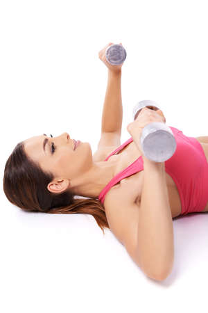 Smiling beautiful young woman exercising with barbells lying on her back raising her arms in the airの写真素材
