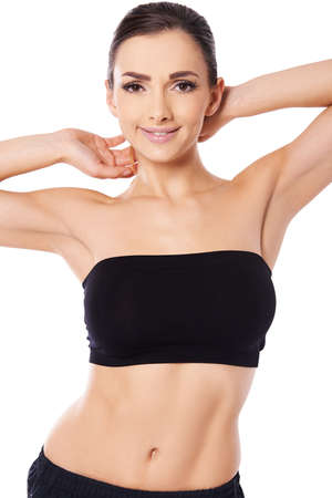 Beautiful sexy brunette woman with a bare midriff posing with her hands behind her head, cropped view studio portrait isolated on whiteの写真素材