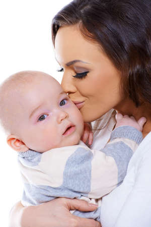 Loving mother with a lovely tender smile on her face kissing her small baby who is looking curiously at the camera, studio portrait isolated on whiteの写真素材