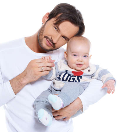Proud young father posing with his baby cradled on his arm, both smiling happily at the camera isolated on whiteの写真素材