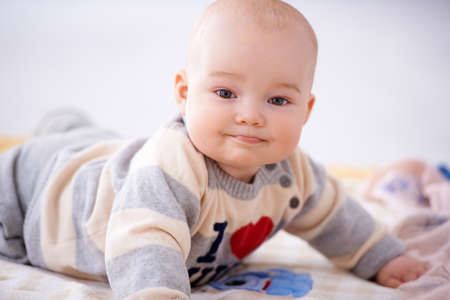 Contented little baby lying on its stomach on a baby blanket raised up on it hands smiling at the cameraの写真素材