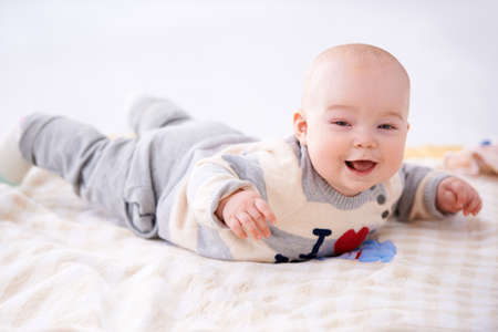 Beautiful laughing baby lying on its stomach on a baby blanket smiling happily at the cameraの写真素材