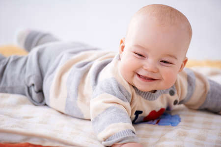 Adorable smiling baby lying on its stomach on a baby blanket facing the cameraの写真素材
