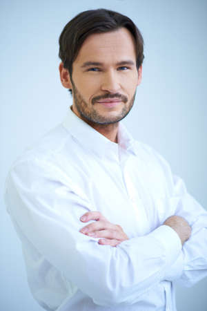 Attractive smiling bearded man in shirtsleeves standing with his arms folded, upper body studio portrait on whiteの写真素材