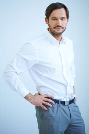Good looking bearded young man standing looking at the camera with a smile with his hands on his hipsの写真素材