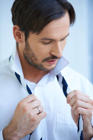 Attractive bearded young man putting on his tie evening out the lengths before tying the knotの写真素材