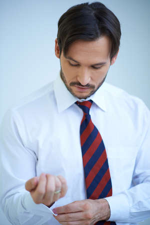 Attractive young man looking down at his arm doing up his shirt cuffs as he dresses ready for a day at the officeの写真素材