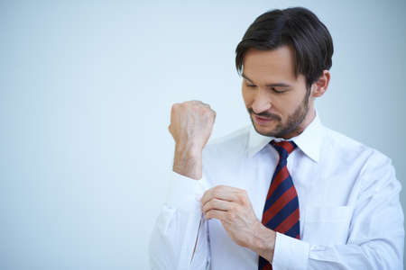 Young man buttoning his cuffs on his shirt as he gets dressed ready for a day at the officeの写真素材
