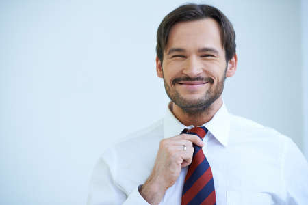 Happy bearded man grinning at the camera as he stands straightening his tieの写真素材