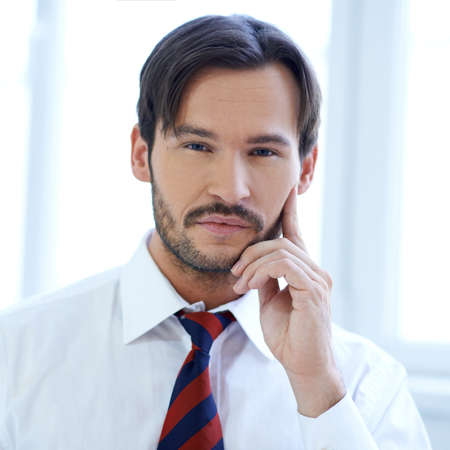 Thoughtful young businessman with his hand raised to his cheek as he looks pensively at the cameraの写真素材