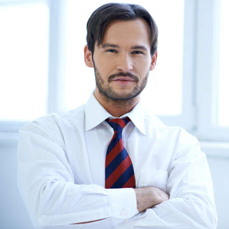 Handsome man standing with folded arms against a bright window with copyspaceの写真素材
