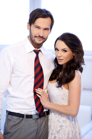 Smiling attractive young couple standing close together looking at the camera against high key windowsの写真素材