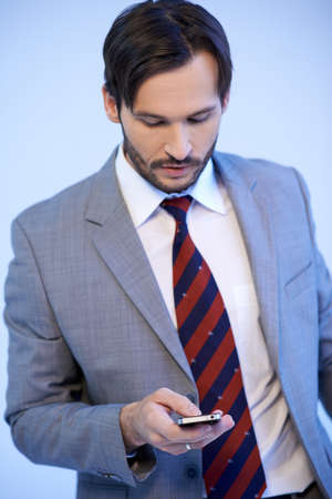 Businessman making a mobile phone call standing looking down at the screen as he selects the numberの写真素材