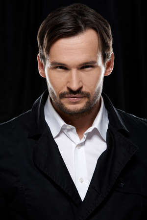 Suave handsome bearded young man in a white shirt and black jacket , head and shoulders studio portrait on a dark backgroundの写真素材
