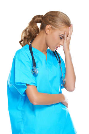 Attractive young female nurse or doctor dressed in scrubs with a stethoscope holding her hand to her head in anguishの写真素材