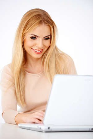 Happy blonde woman working on a laptop at her deskの写真素材