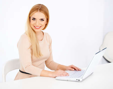 Smiling sexy blonde woman looking at camera and working on a laptop at her deskの写真素材