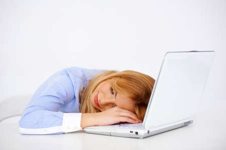 Beautiful young blonde woman daydreaming smiling with her head on the laptop at her deskの写真素材