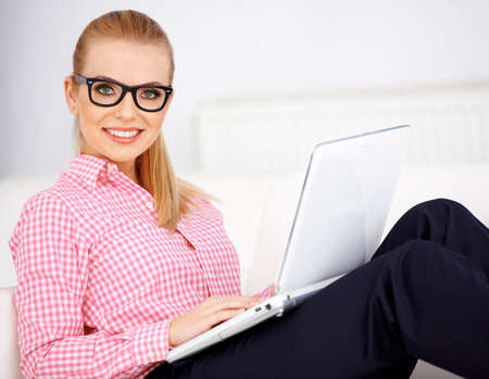 Blond girl wearing black glasses, sitting with laptop and smilingの写真素材
